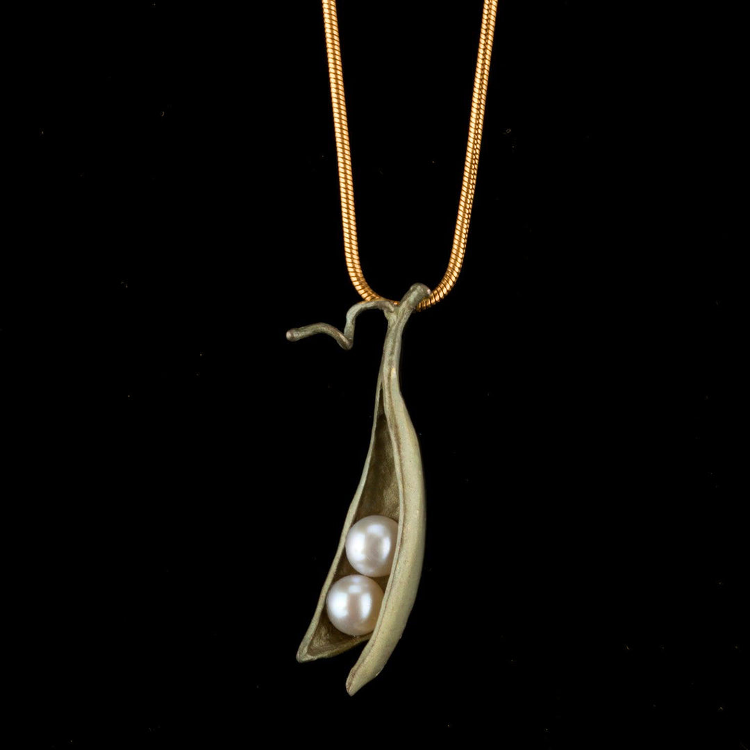 Gold necklace with a pea pod pendant featuring two pearls on a black background