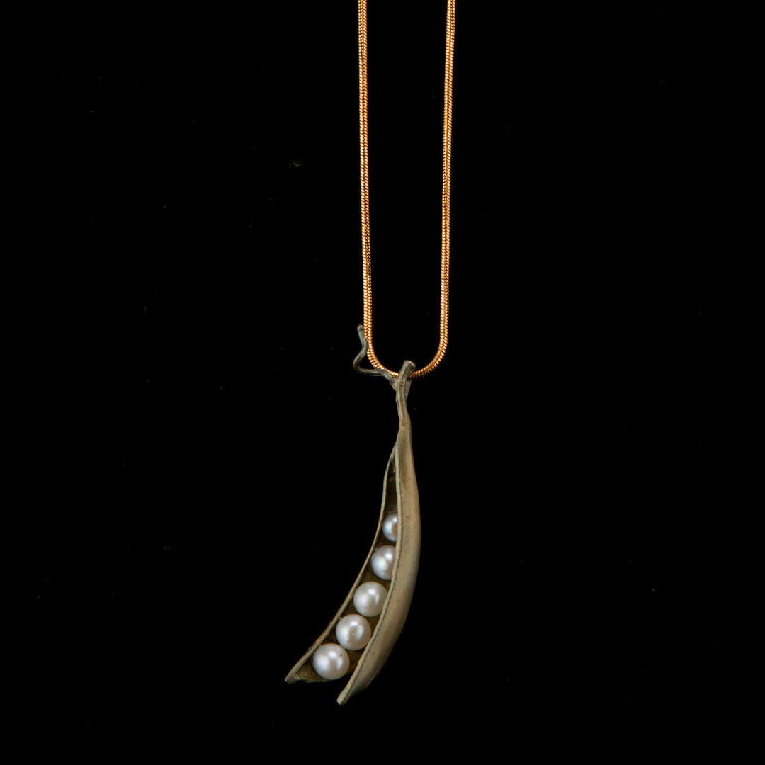 Gold necklace with a pea pod pendant containing pearls on a black background