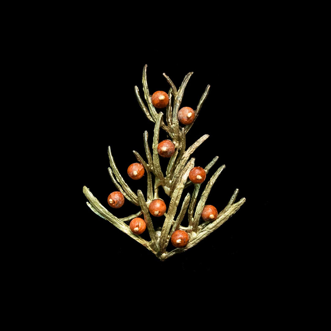 A small green-toned branch brooch with multiple round orange-red berries, centered on a solid black background.