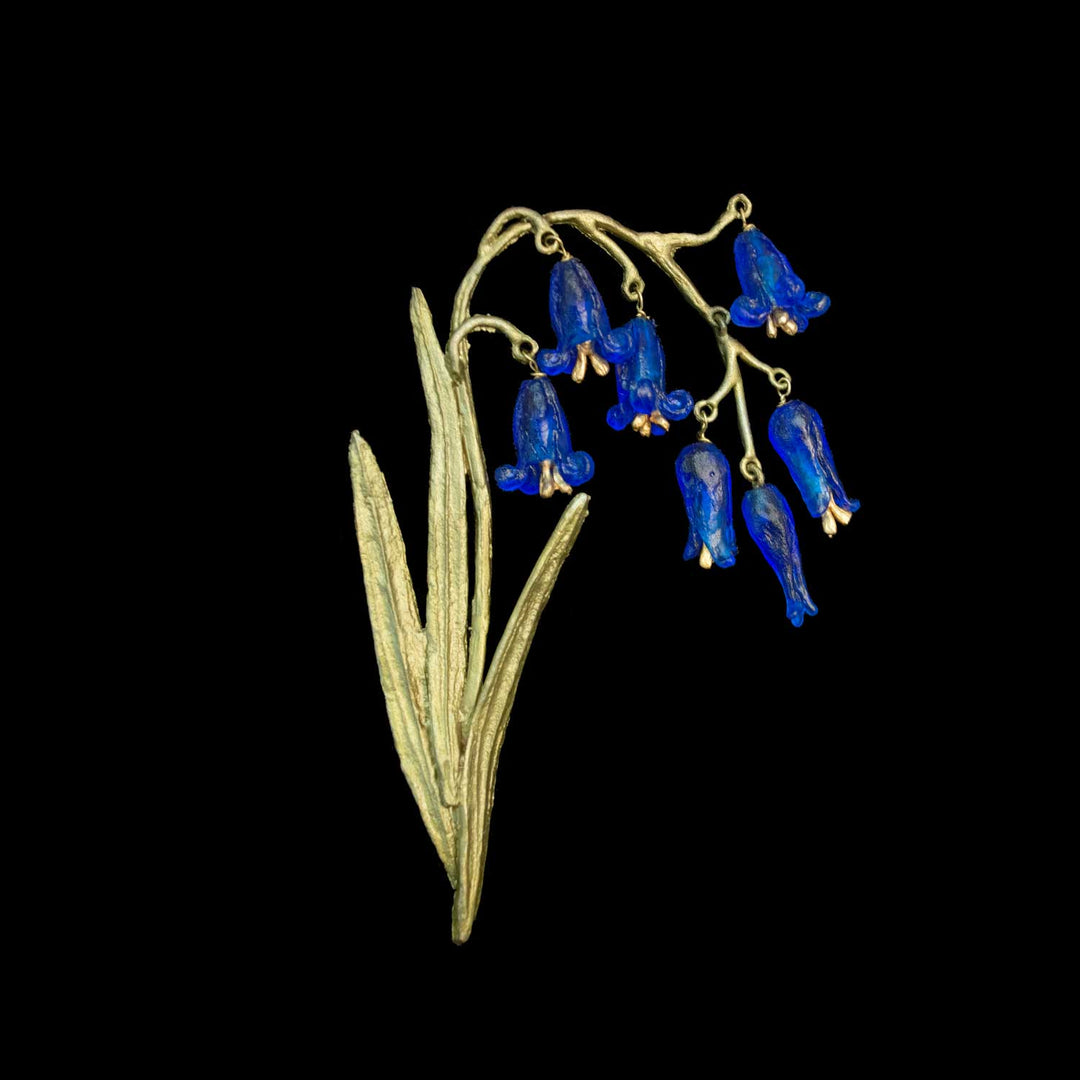A green-tone floral brooch featuring dangling blue bell-shaped flowers and elongated leaves, shown on a solid black background.