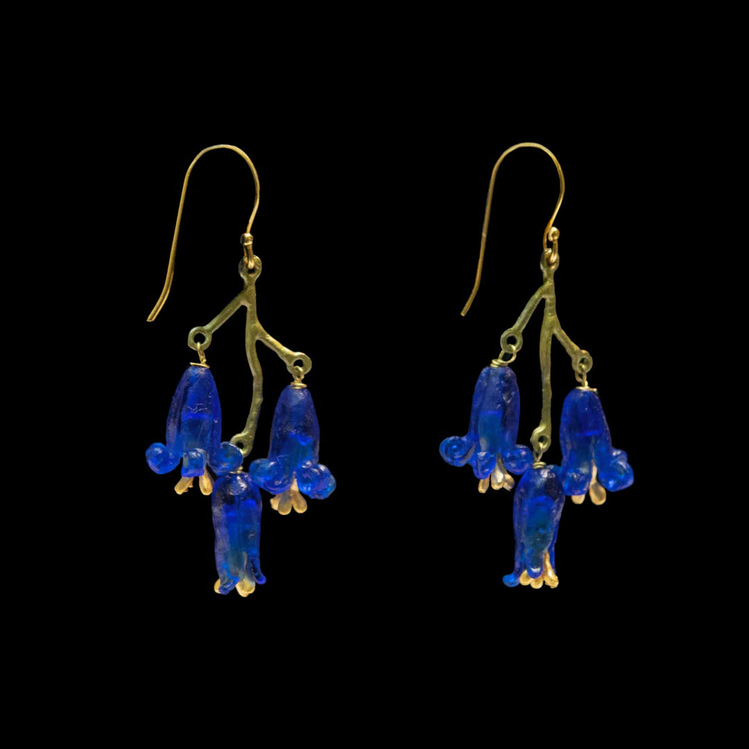 A pair of dangling earrings with green-tone branch-shaped hooks and blue bell-shaped glass drops, shown against a solid black background.