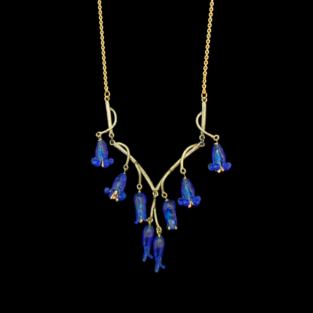 A gold  and green necklace featuring decorative eight dangling blue bell-shaped glass flowers on a black background.