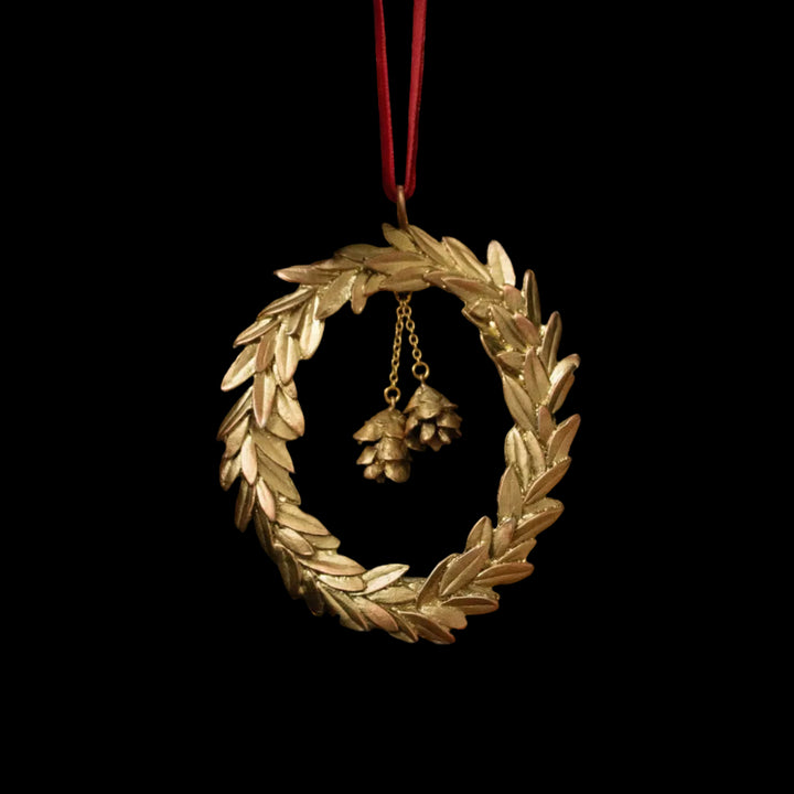 Gold wreath ornament with pine cones hanging on a Christmas tree.