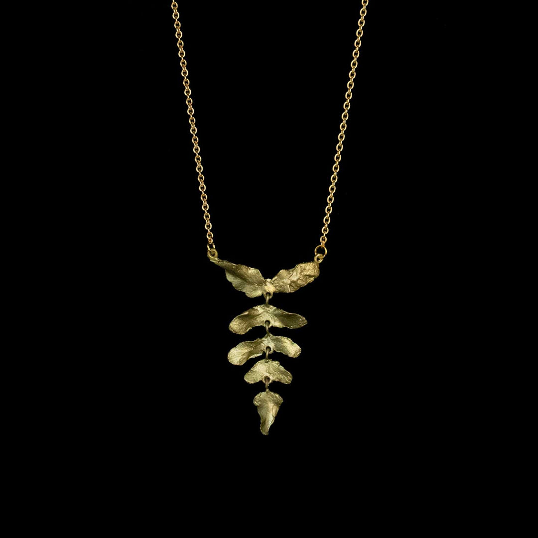A green leaf pendant necklace on a delicate gold chain, displayed against a solid black background.