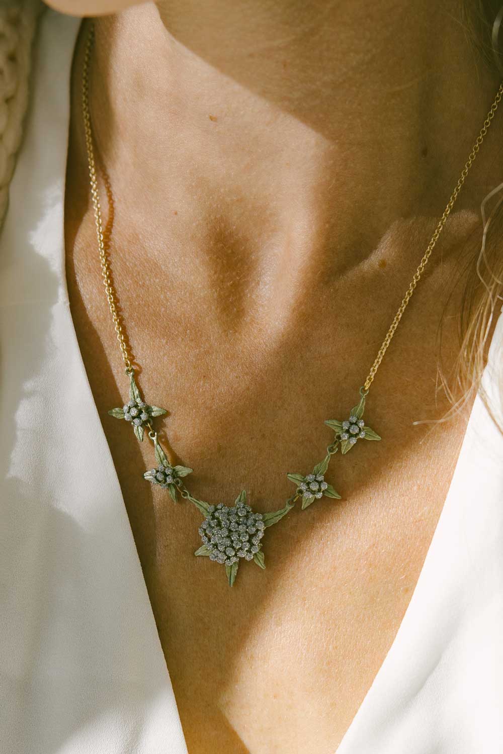 A woman wearing the Queen Anne's Lace necklace. Her décolleté is visible with the edges of her white top showing.