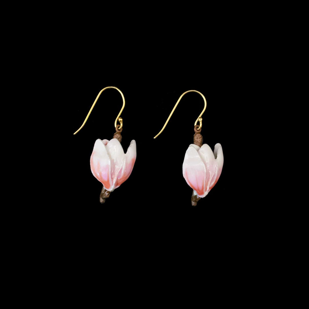 A pair of dangling earrings shaped like small pink and white blossoms on brown branches, suspended from gold fishhook wires, shown against a solid black background.