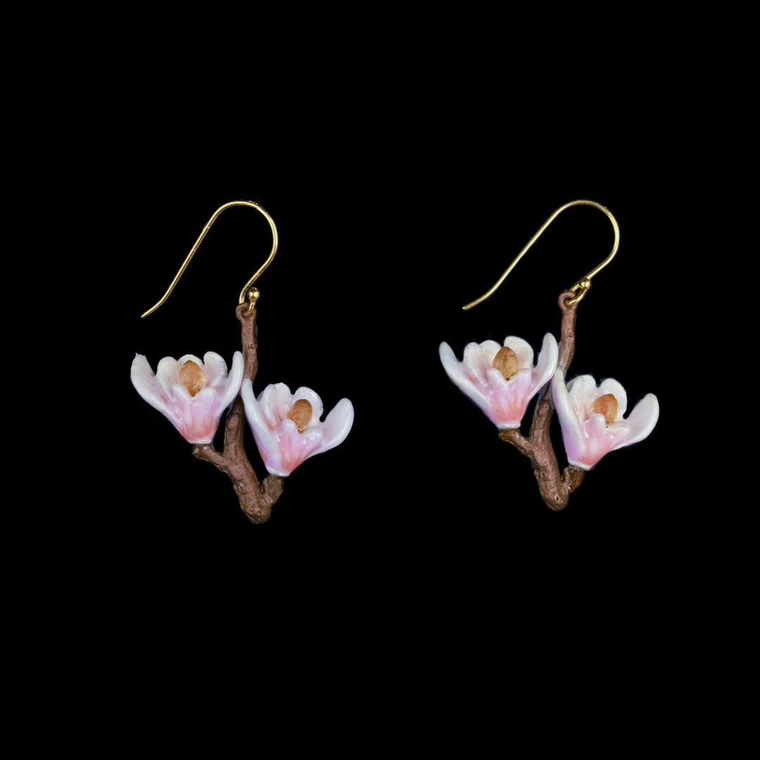 A pair of dangling earrings shaped like small pink and white blossoms on brown branches, suspended from gold fishhook wires, shown against a solid black background.