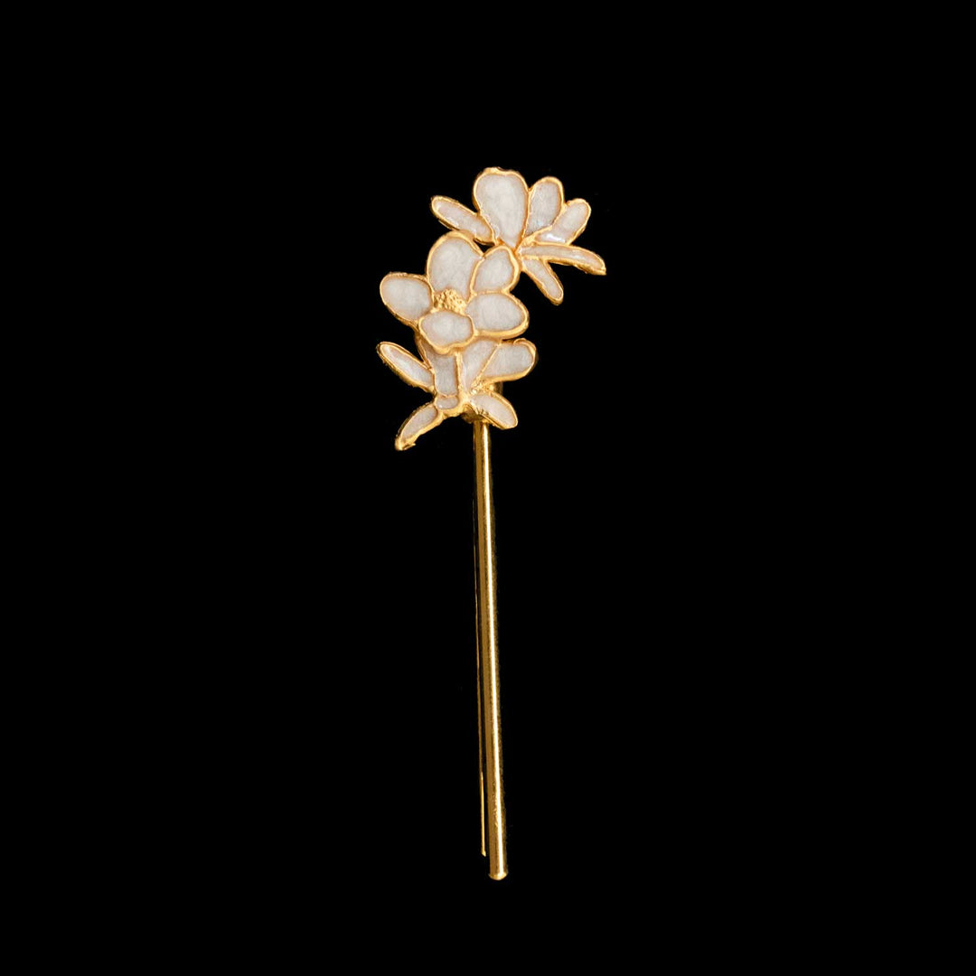 A gold-tone floral hair pin with white enamel petals, shown against a solid black background.