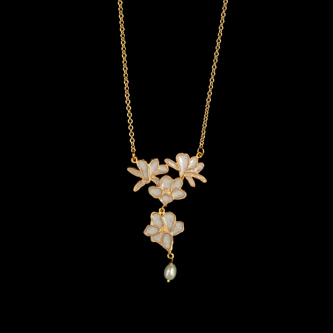 A gold-tone necklace featuring three cascading flower motifs with iridescent white enamel and a small dangling pearl bead, shown against a solid black background.