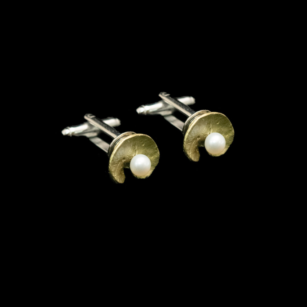 A pair of green and silver cufflinks, each featuring a textured gold crescent shape with a small white pearl at the center, set against a solid black background.