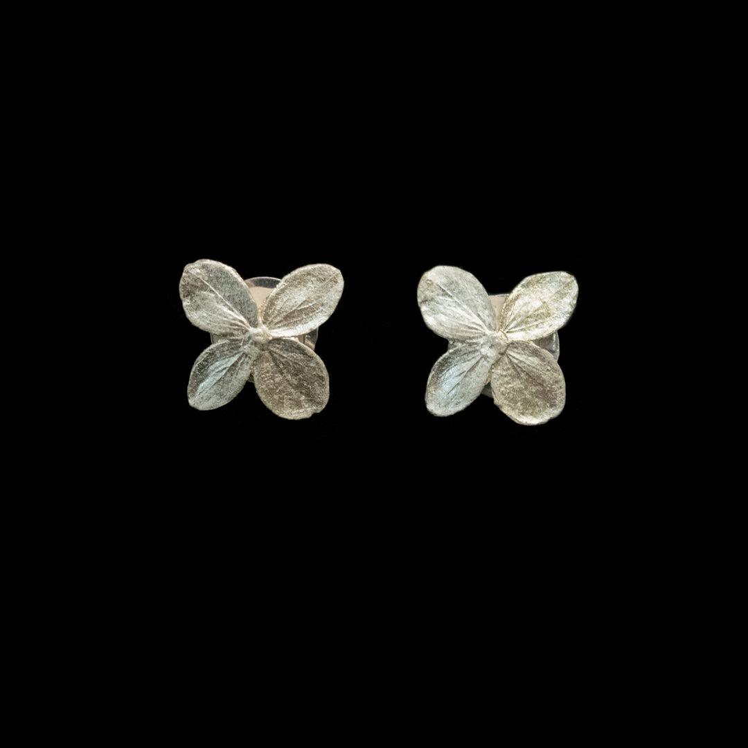A pair of silver-toned flower cufflinks with four textured petals, displayed on a solid black background.