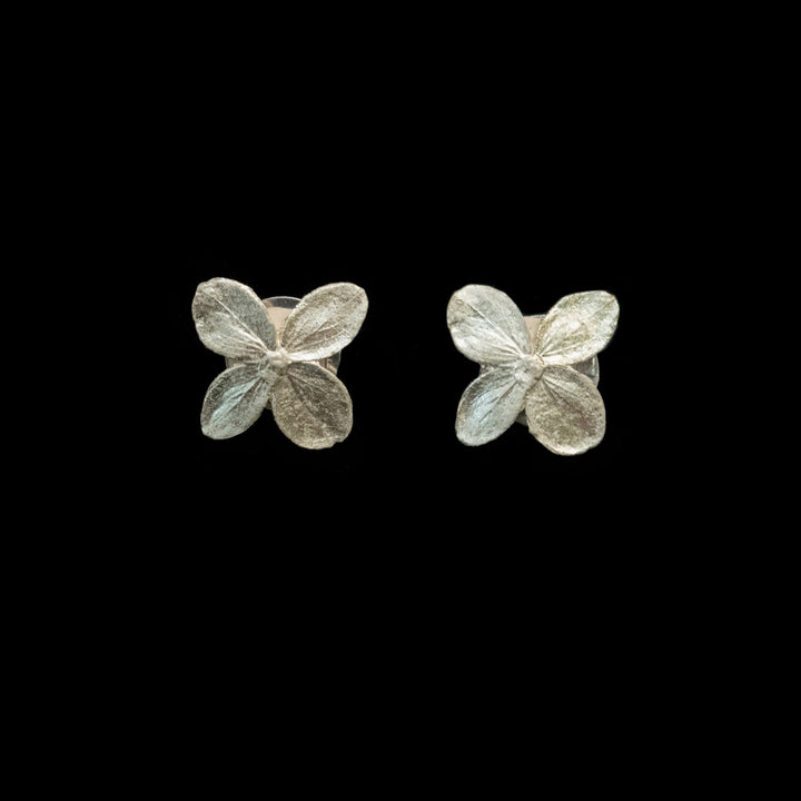 A pair of silver-toned flower cufflinks with four textured petals, displayed on a solid black background.
