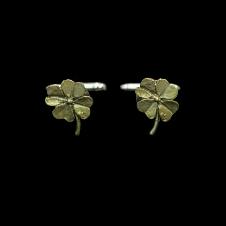A pair of small four-leaf clover cufflinks with a textured metallic finish, shown against a solid black background.