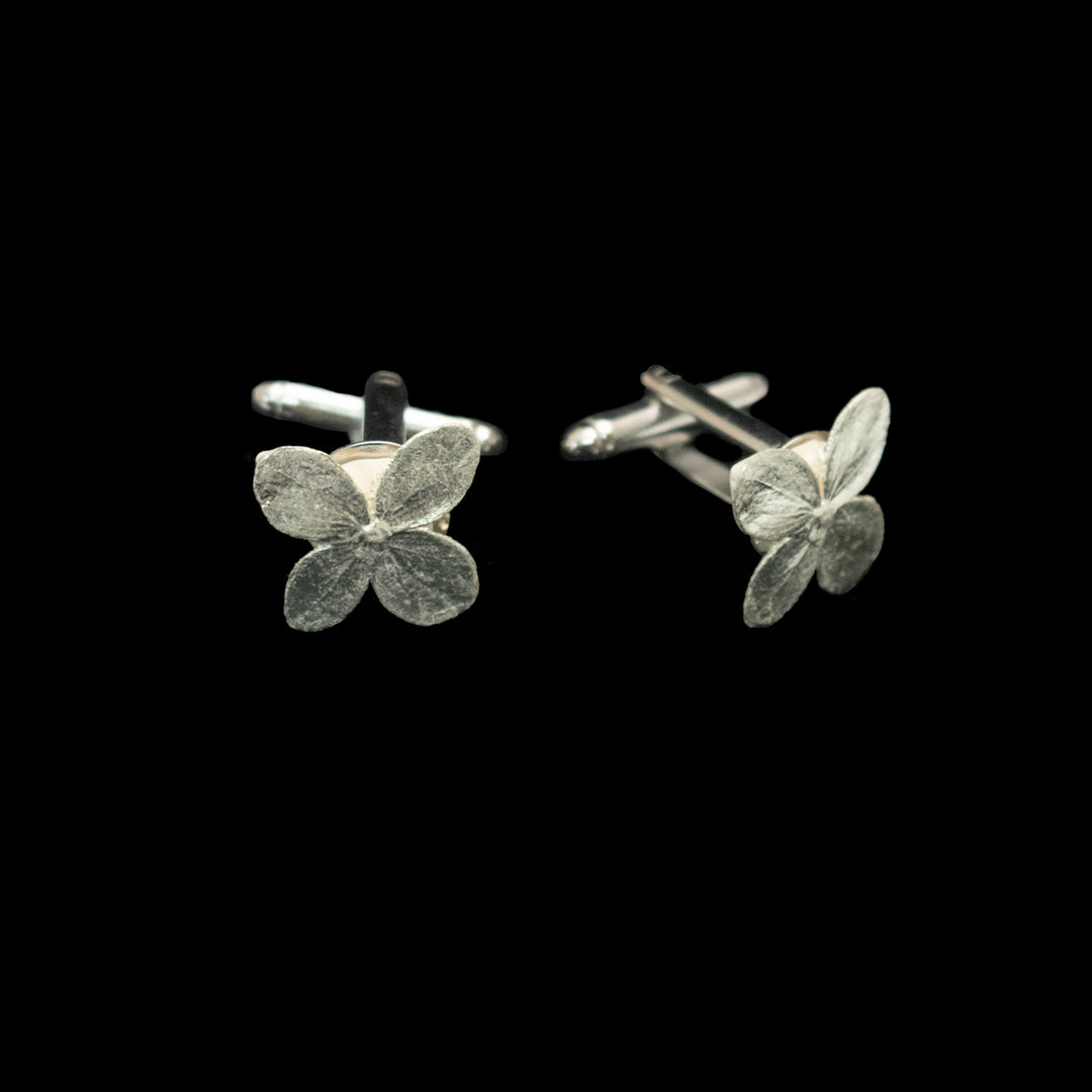 A pair of silver-toned flower-shaped cufflinks on a solid black background.