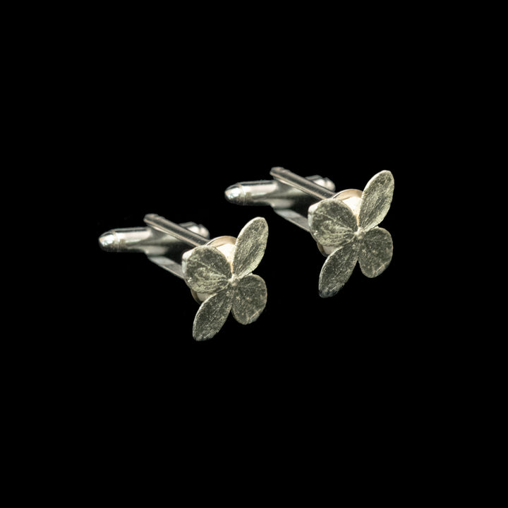 A pair of silver four-petal flower cufflinks on a solid black background.